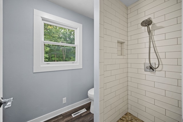 bathroom with wood-type flooring, a healthy amount of sunlight, tiled shower, and toilet