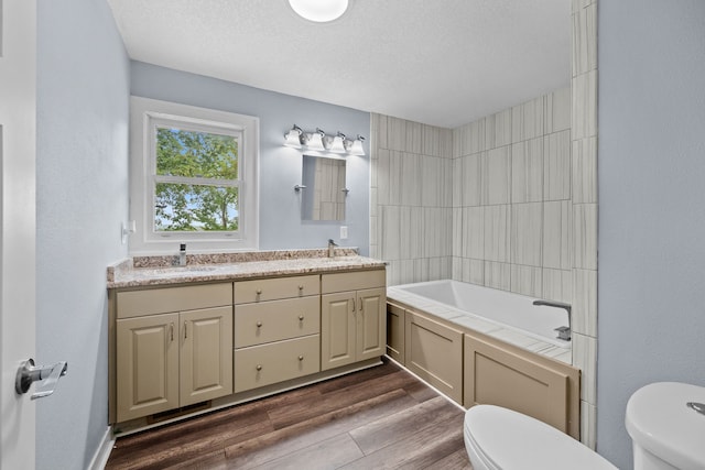 full bath with double vanity, toilet, wood finished floors, a textured ceiling, and a sink