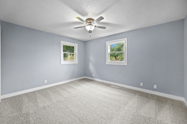 carpeted empty room with a ceiling fan, baseboards, visible vents, and a wealth of natural light