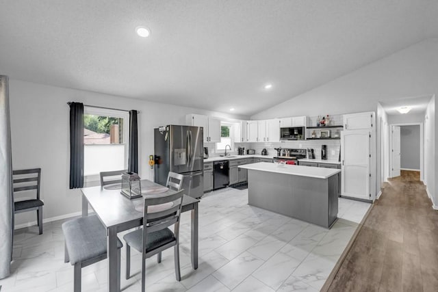 kitchen with a kitchen island, marble finish floor, vaulted ceiling, stainless steel appliances, and light countertops