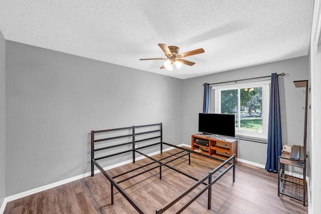 bedroom featuring a textured ceiling, baseboards, and wood finished floors