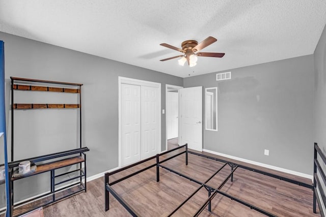 bedroom with a textured ceiling, wood finished floors, visible vents, baseboards, and a closet