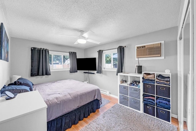 bedroom with multiple windows, a wall unit AC, baseboard heating, and wood finished floors