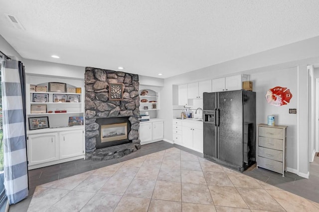 kitchen featuring a textured ceiling, a fireplace, a sink, black fridge with ice dispenser, and white cabinetry