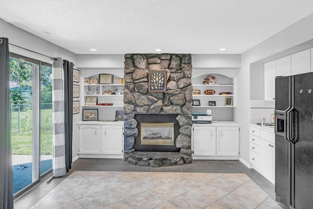 kitchen with a textured ceiling, a stone fireplace, black fridge with ice dispenser, white cabinetry, and light countertops