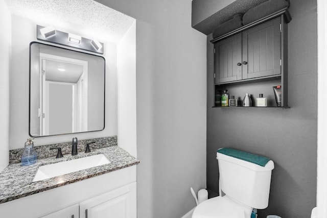 half bath featuring vanity, toilet, and a textured ceiling