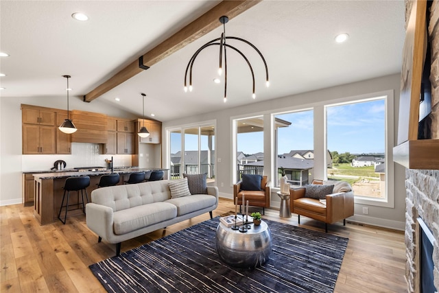 living area featuring light wood-style floors, a healthy amount of sunlight, vaulted ceiling with beams, and a stone fireplace