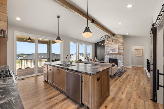 kitchen featuring a barn door, lofted ceiling with beams, stainless steel appliances, light wood-style floors, and a sink