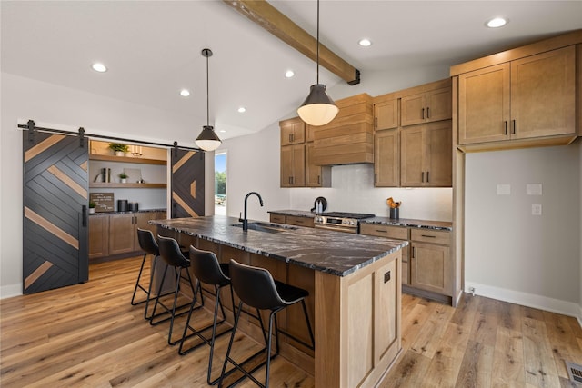 kitchen featuring vaulted ceiling with beams, a barn door, a sink, light wood-style floors, and gas stove