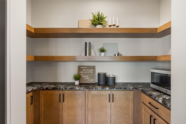 kitchen featuring stainless steel microwave, open shelves, and dark stone counters