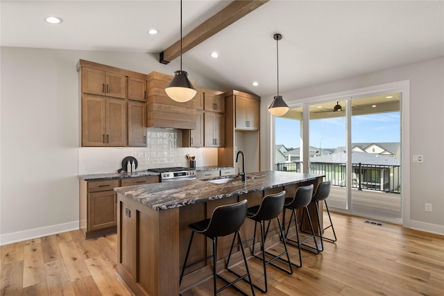 kitchen featuring lofted ceiling with beams, stainless steel gas range oven, a sink, light wood-style floors, and decorative backsplash