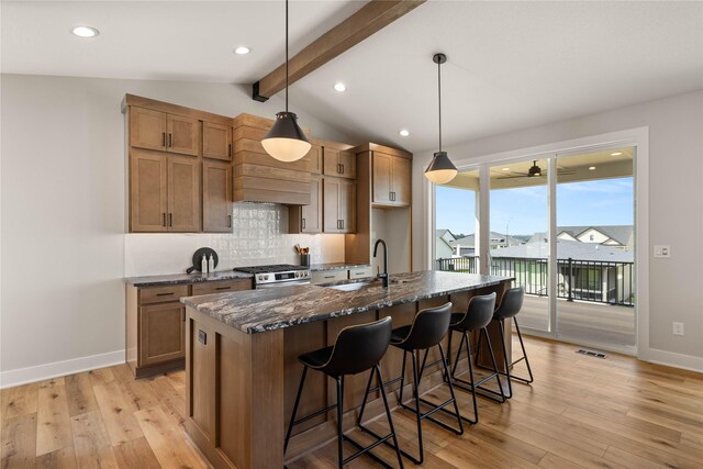 1185 NW 28th St, Grimes, IA 50111 - kitchen featuring a sink, stainless steel range with gas stovetop, tasteful backsplash, an island with sink, and light wood-type flooring
