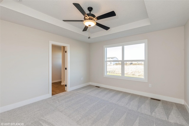 spare room featuring ceiling fan, carpet floors, and a tray ceiling