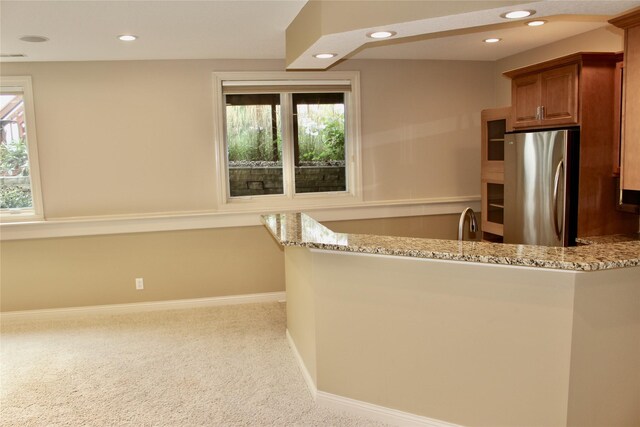 kitchen featuring light carpet, kitchen peninsula, stainless steel fridge, and light stone counters