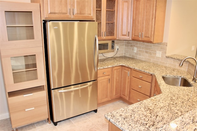 kitchen with light stone counters, backsplash, appliances with stainless steel finishes, glass insert cabinets, and a sink