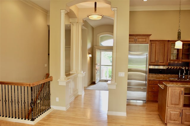 kitchen with built in fridge, brown cabinetry, decorative columns, and a sink