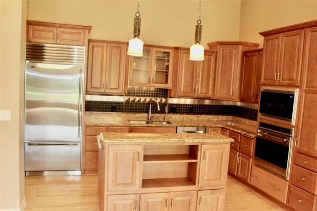 kitchen with built in appliances, backsplash, light hardwood / wood-style floors, light stone countertops, and a center island