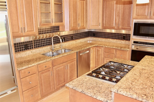 kitchen featuring a sink, appliances with stainless steel finishes, decorative backsplash, light stone countertops, and glass insert cabinets