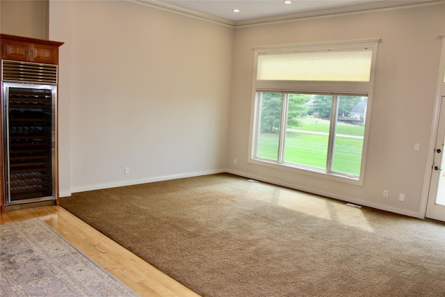 unfurnished living room featuring recessed lighting, beverage cooler, wood finished floors, baseboards, and ornamental molding