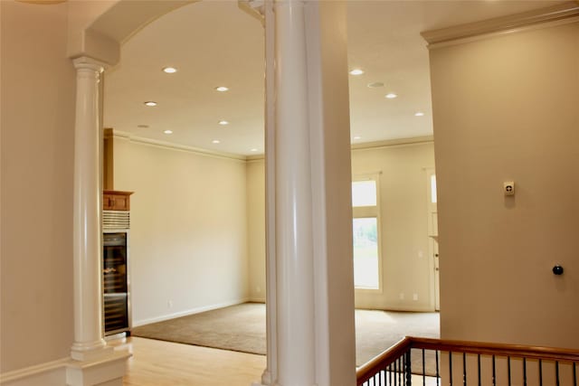 corridor with decorative columns, arched walkways, light colored carpet, and ornamental molding