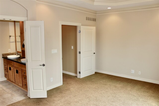 unfurnished bedroom featuring sink, ornamental molding, ensuite bath, a raised ceiling, and light colored carpet