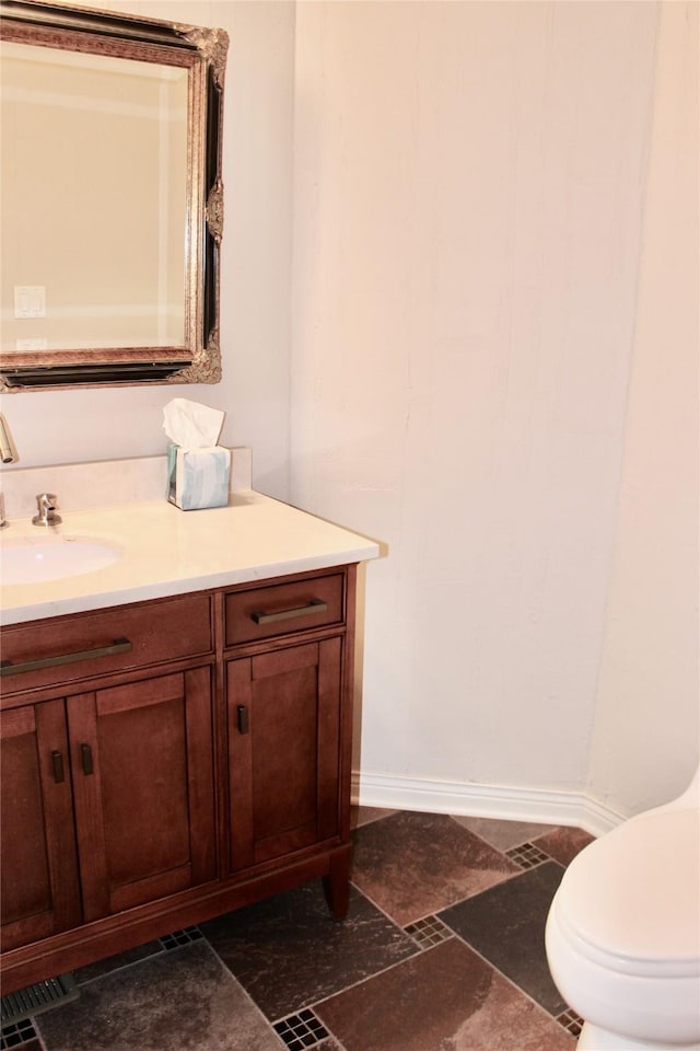 bathroom featuring toilet, stone finish floor, vanity, and baseboards