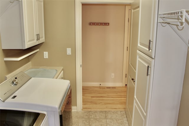 laundry room featuring light hardwood / wood-style floors, washing machine and dryer, and cabinets