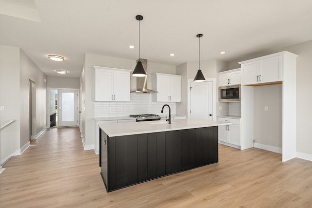 kitchen with a center island with sink, white cabinets, sink, hanging light fixtures, and decorative backsplash