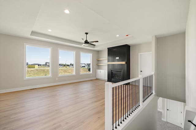 unfurnished living room with hardwood / wood-style floors, a raised ceiling, and ceiling fan