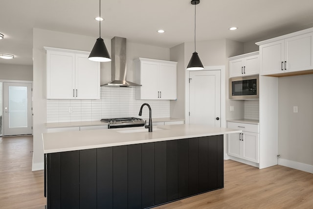 kitchen with sink, hanging light fixtures, wall chimney exhaust hood, built in microwave, and an island with sink