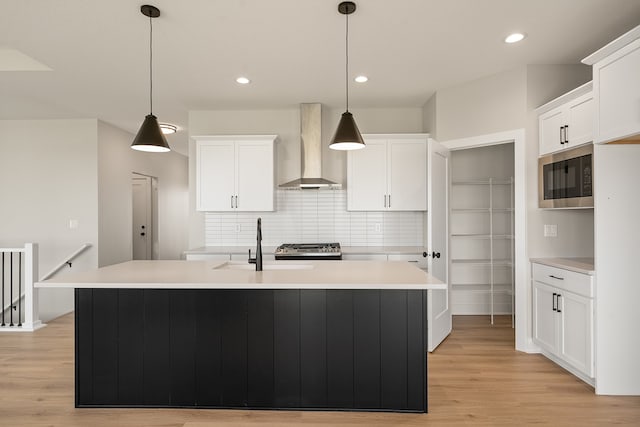 kitchen featuring wall chimney exhaust hood, built in microwave, a kitchen island with sink, white cabinetry, and hanging light fixtures