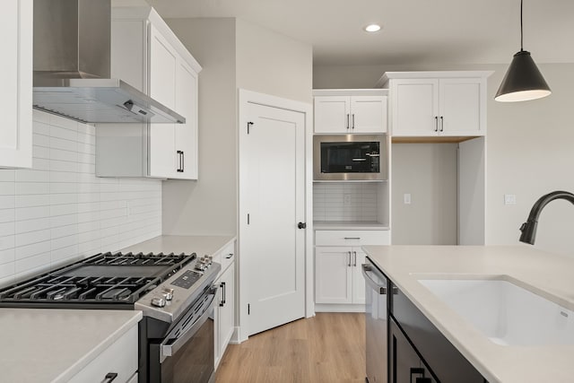 kitchen featuring sink, wall chimney range hood, pendant lighting, white cabinets, and appliances with stainless steel finishes