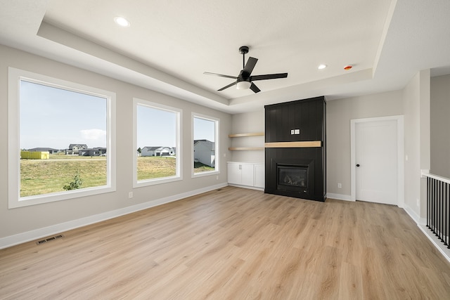 unfurnished living room with a tray ceiling, ceiling fan, a large fireplace, and light hardwood / wood-style floors