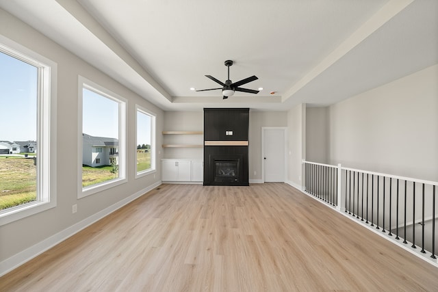 unfurnished living room featuring a tray ceiling, a large fireplace, a healthy amount of sunlight, and light hardwood / wood-style flooring