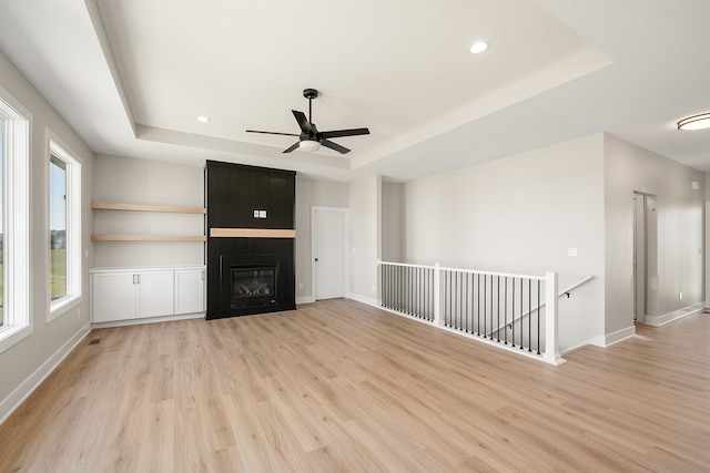 unfurnished living room with a fireplace, light wood-type flooring, and a tray ceiling