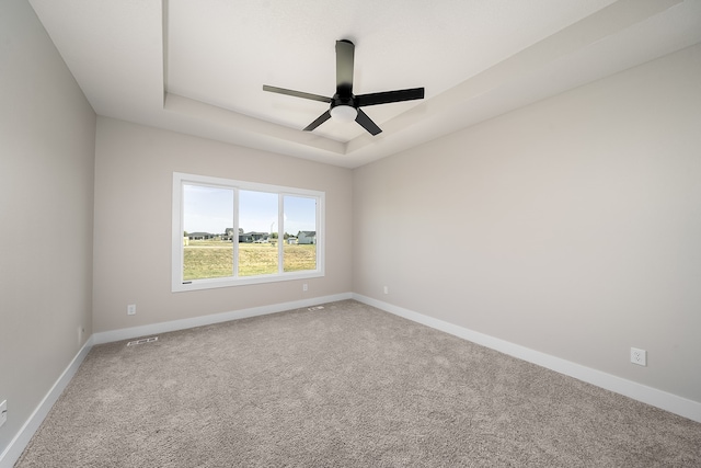 empty room with a tray ceiling, ceiling fan, and carpet floors