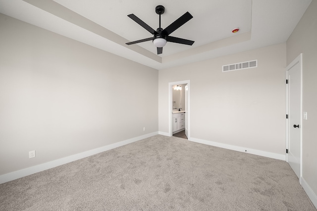 unfurnished bedroom featuring carpet, ceiling fan, ensuite bathroom, and a tray ceiling