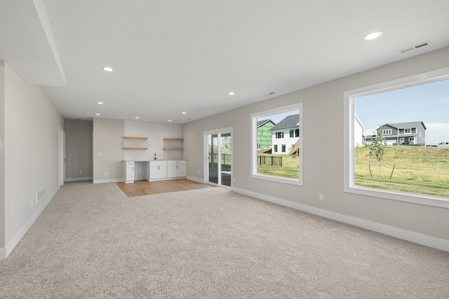 unfurnished living room featuring light carpet and a healthy amount of sunlight