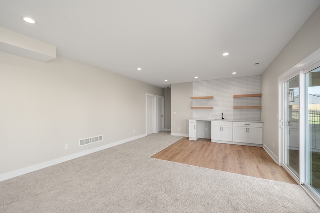 unfurnished living room with light carpet, sink, and built in desk