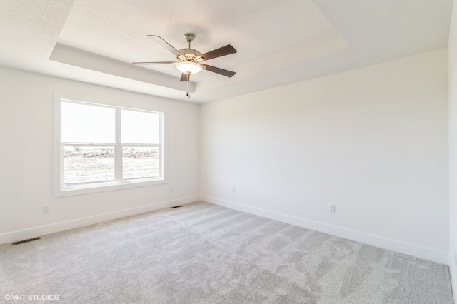 carpeted spare room featuring ceiling fan and a raised ceiling