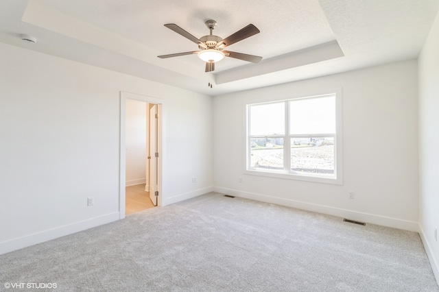 carpeted empty room with ceiling fan and a raised ceiling