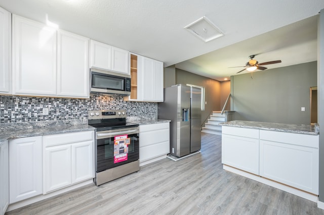 kitchen with light hardwood / wood-style flooring, appliances with stainless steel finishes, white cabinetry, light stone counters, and tasteful backsplash