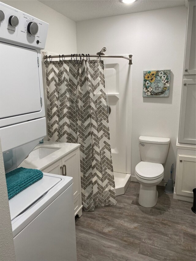 bathroom with stacked washer / dryer, toilet, a stall shower, wood finished floors, and a textured ceiling