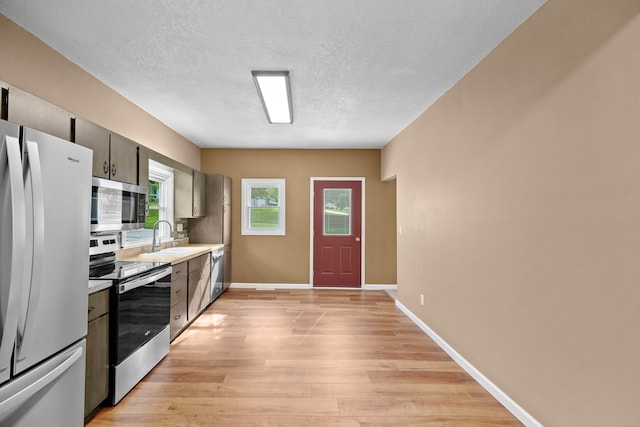 kitchen featuring light wood-type flooring, a textured ceiling, appliances with stainless steel finishes, and sink