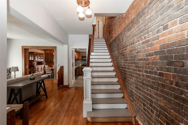 stairway with hardwood / wood-style floors, brick wall, and a textured ceiling