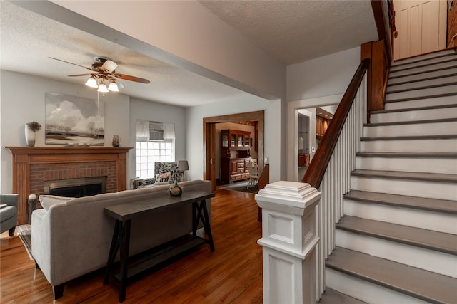 living room with ceiling fan, a fireplace, a textured ceiling, and dark hardwood / wood-style floors