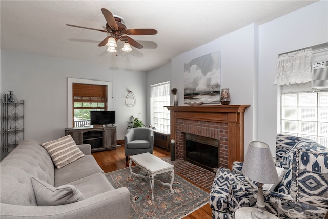 living room with a textured ceiling, ceiling fan, wood-type flooring, and a brick fireplace