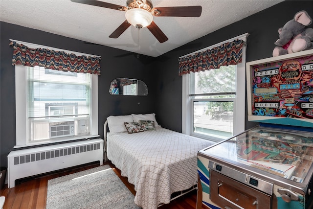 bedroom with radiator heating unit, cooling unit, a textured ceiling, dark wood-type flooring, and ceiling fan