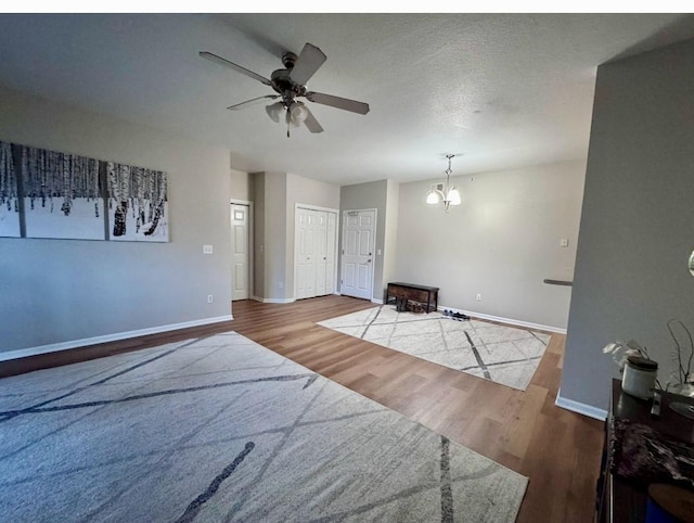 unfurnished living room with a textured ceiling, baseboards, wood finished floors, and ceiling fan with notable chandelier