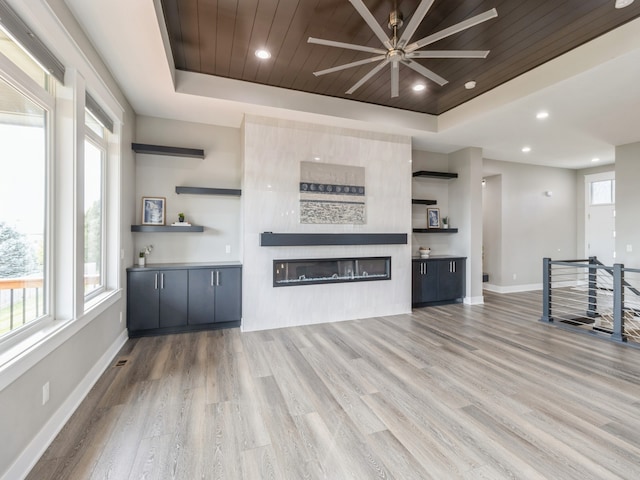 unfurnished living room featuring a fireplace, ceiling fan, light hardwood / wood-style floors, and a raised ceiling